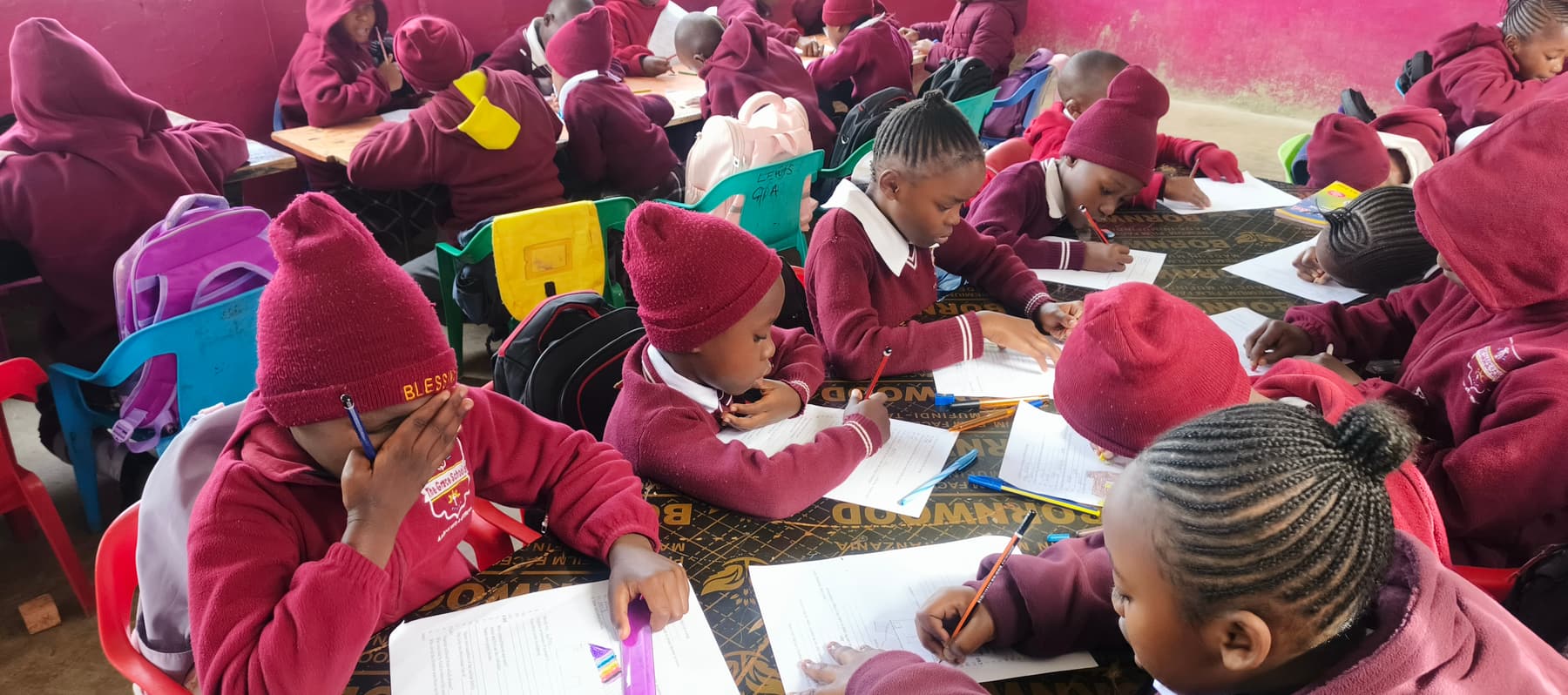 Pre-Primary learners in crimson uniforms working at their desks