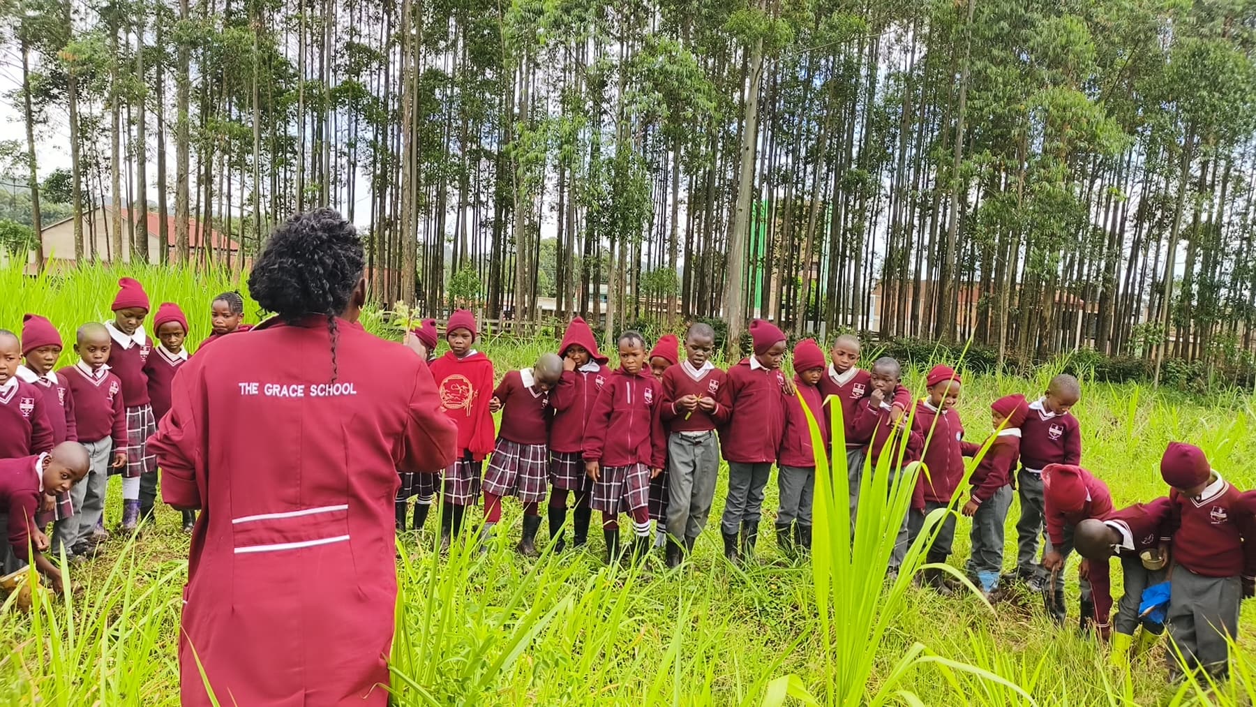 A teacher in a Grace Schools coat leading her class through the grass on the school grounds